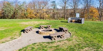 a fire pit with wooden tables and benches in a field